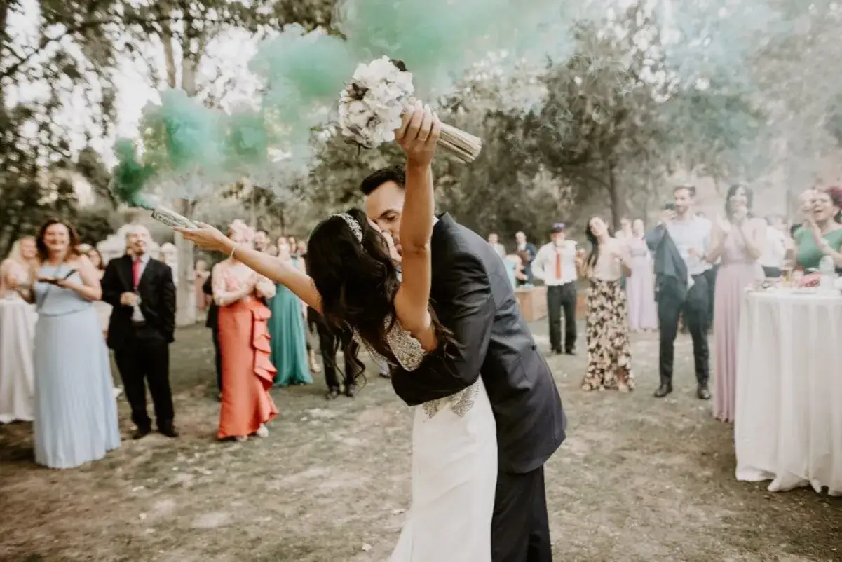 Novios bes&aacute;ndose con humo verde y ramo de flores. Una celebraci&oacute;n de bodas low cost llena de alegr&iacute;a y color.