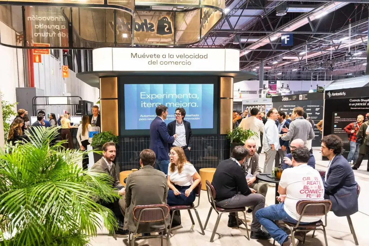Gente conversando en un evento comercial, con una pantalla que dice 