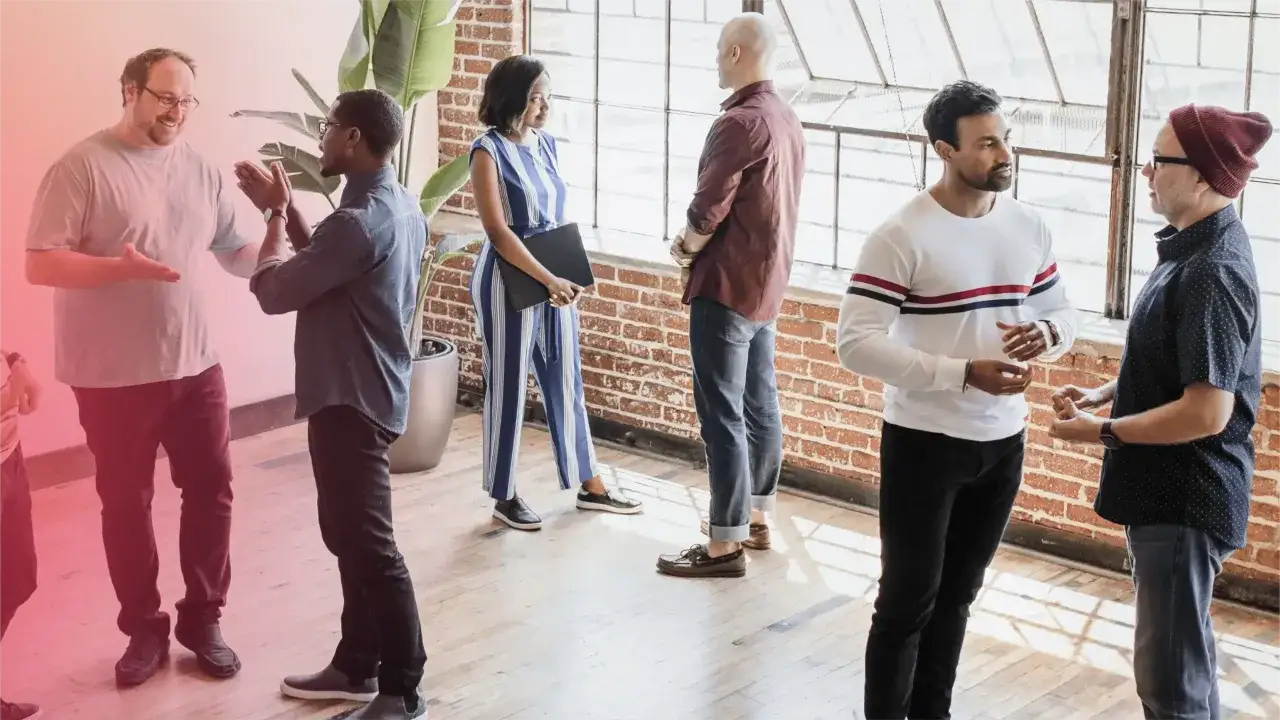Un grupo diverso de personas participa en din&aacute;micas de grupo para empresas, interactuando y colaborando en un espacio luminoso.