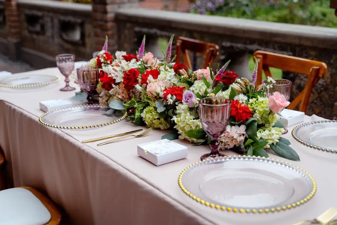 Mesa decorada para una boda civil sencilla y barata. Flores rojas, rosas y verdes, copas moradas y vajilla dorada.