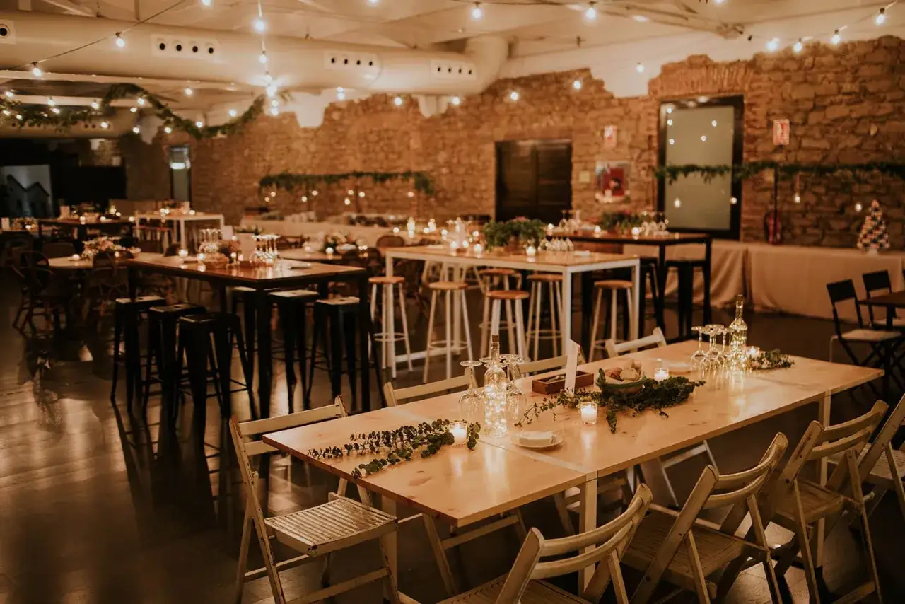 Ambiente r&uacute;stico con luces c&aacute;lidas y mesas decoradas con vegetaci&oacute;n. Perfectas ideas para cenas de empresa inolvidables.