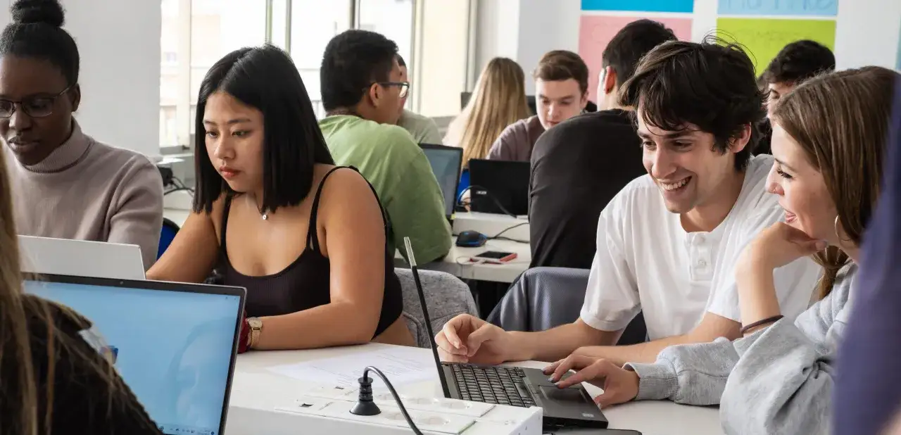 Estudiantes concentrados en un curso de administraci&oacute;n y finanzas, trabajando en sus laptops en un aula moderna.