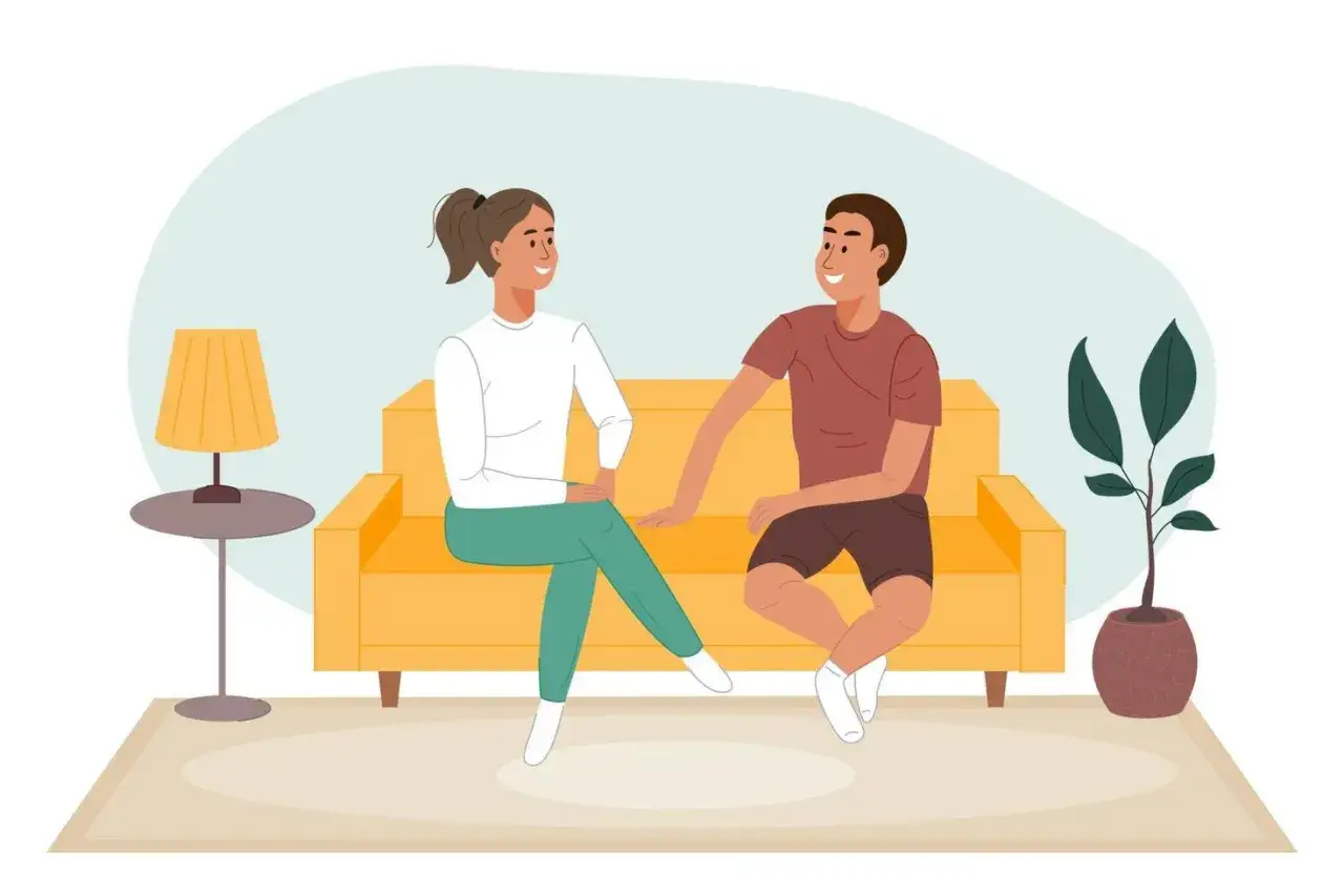 Pareja conversando en un sof&aacute; amarillo, mostrando c&oacute;mo debe ser una relaci&oacute;n de pareja: comunicaci&oacute;n y cercan&iacute;a.