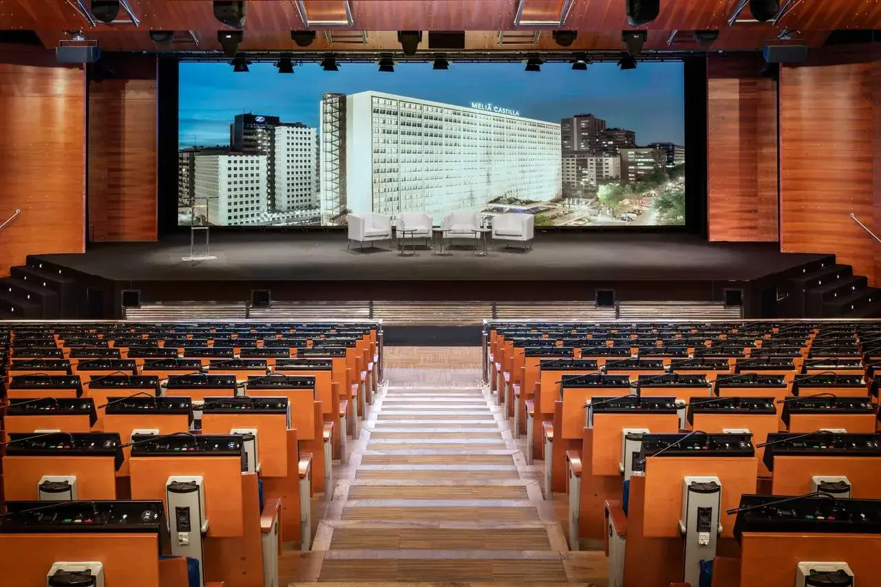 Sala de conferencias lista para un evento de turismo MICE. Butacas, escenario con pantalla gigante y mobiliario moderno.