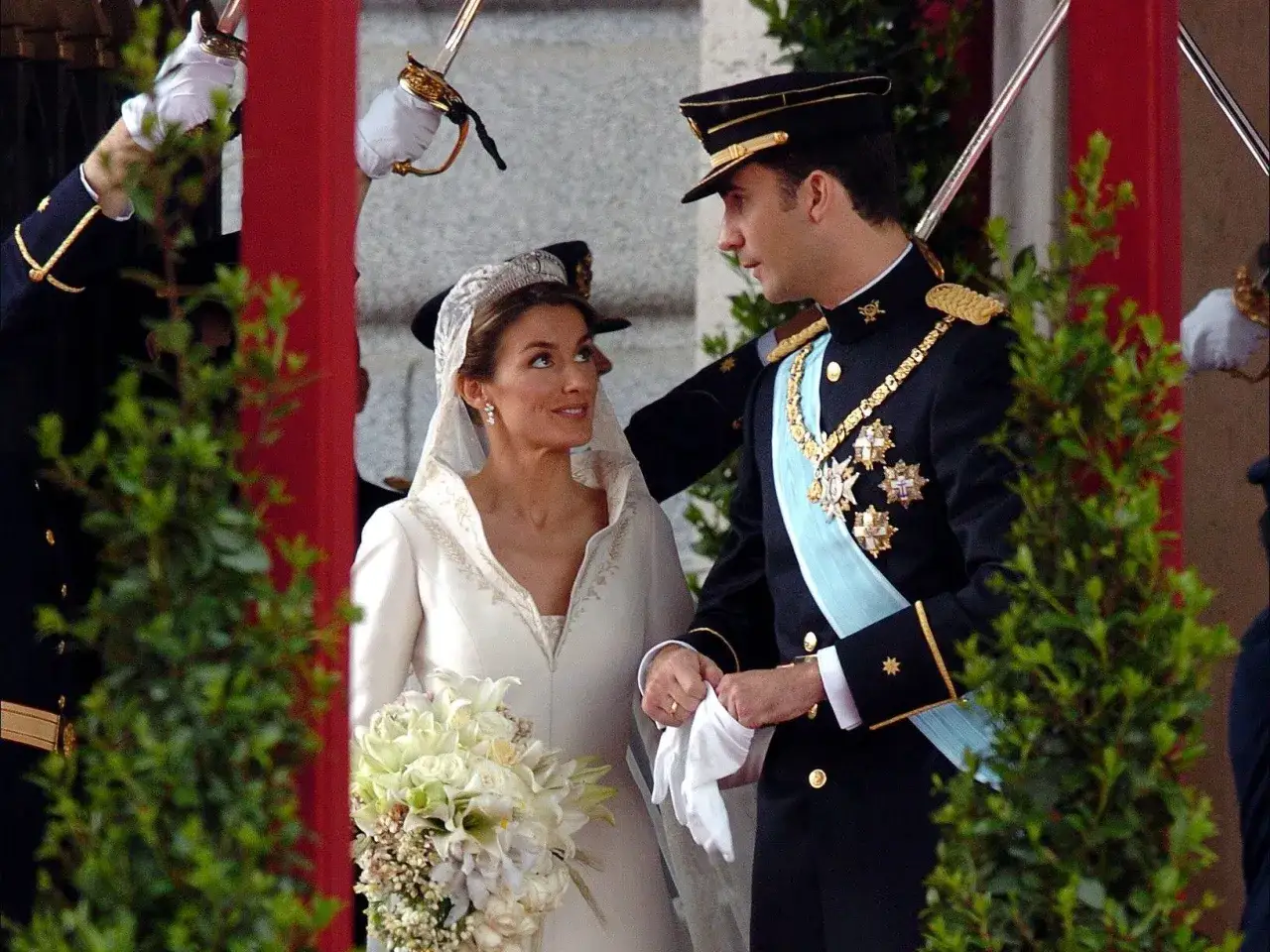 Novios en su boda, un día que celebra bodas de plata, oro y platino. Ella, radiante con velo y ramo; él, con uniforme militar.