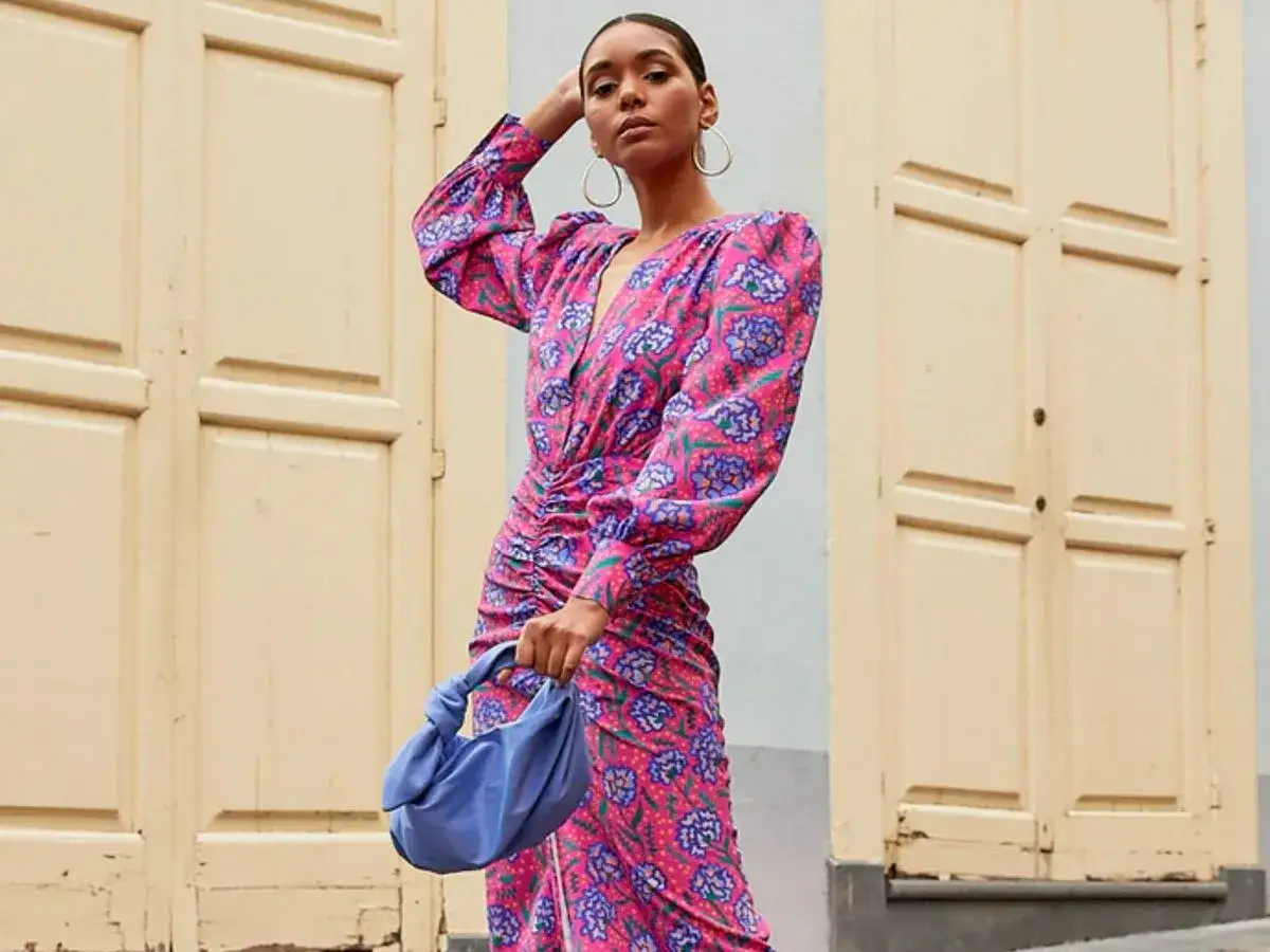 Mujer con vestido estampado floral rosa y azul, ideal para el dress code bodas. Bolso azul y pendientes grandes.