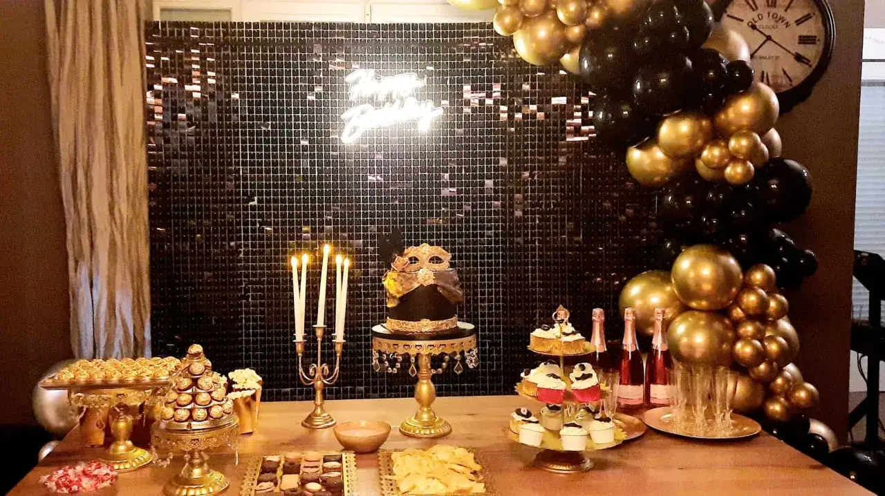 Mesa de dulces para fiesta cumpleaños adultos divertidas con pastel temático, cupcakes, chocolates y globos dorados y negros.