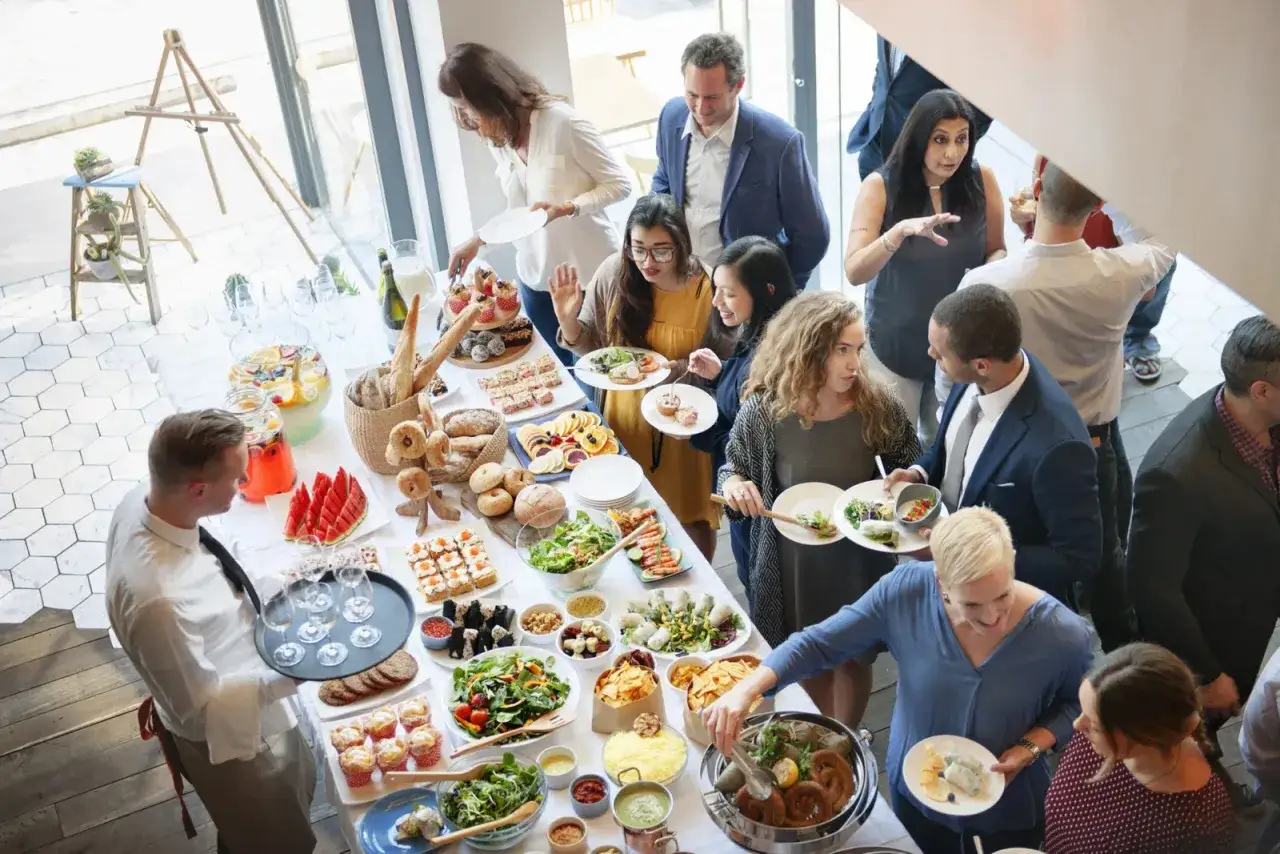 Gente disfrutando de un buffet en fiestas de empresa, con variedad de comida y bebidas.