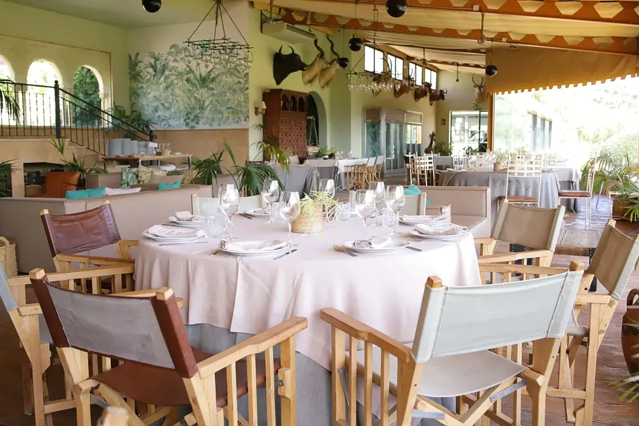 Elegante salón con mesas puestas, ideal para celebrar bautizo. Decoración con plantas y detalles rústicos.