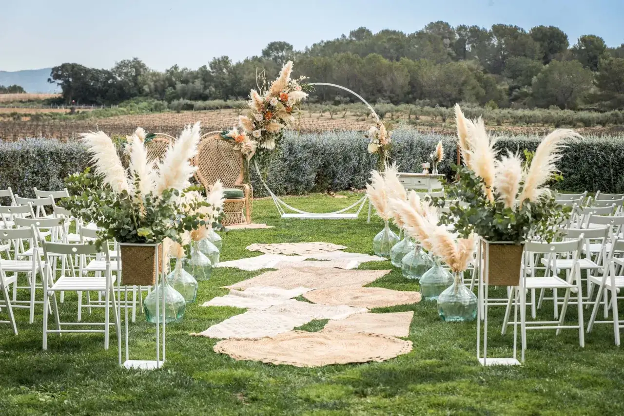 Escenario de boda civil informal con sillas blancas, camino de alfombras de yute, arco floral y pampas. &iexcl;Ideas perfectas para tu gran d&iacute;a!