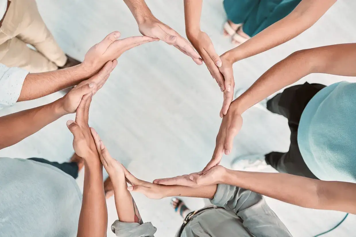 Manos unidas formando un c&iacute;rculo, s&iacute;mbolo de unidad y colaboraci&oacute;n en un workshop de empresa.