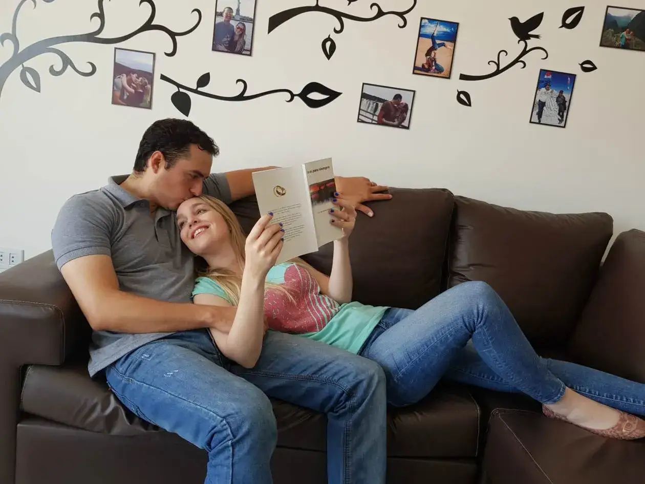 Pareja relajada en un sof&aacute; leyendo libros de terapia de pareja. &Eacute;l le da un beso en la frente.