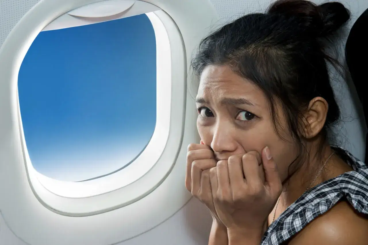 Mujer con miedo a volar, mordi&eacute;ndose las u&ntilde;as junto a la ventana del avi&oacute;n. Busca frases para perder el miedo a volar.