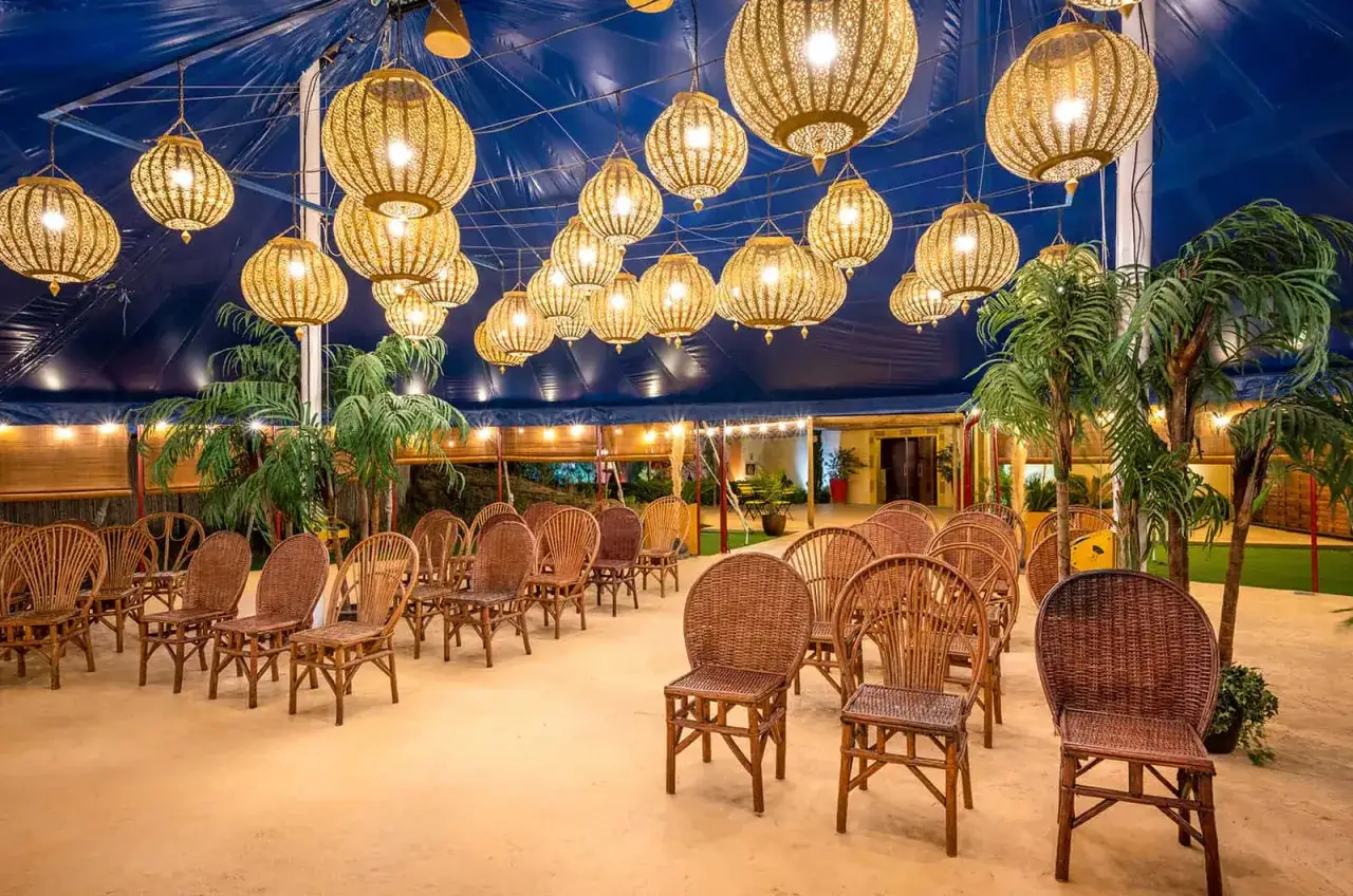 Sillas de mimbre dispuestas para un evento bajo l&aacute;mparas doradas. Un hermoso escenario para tus sitios de eventos.