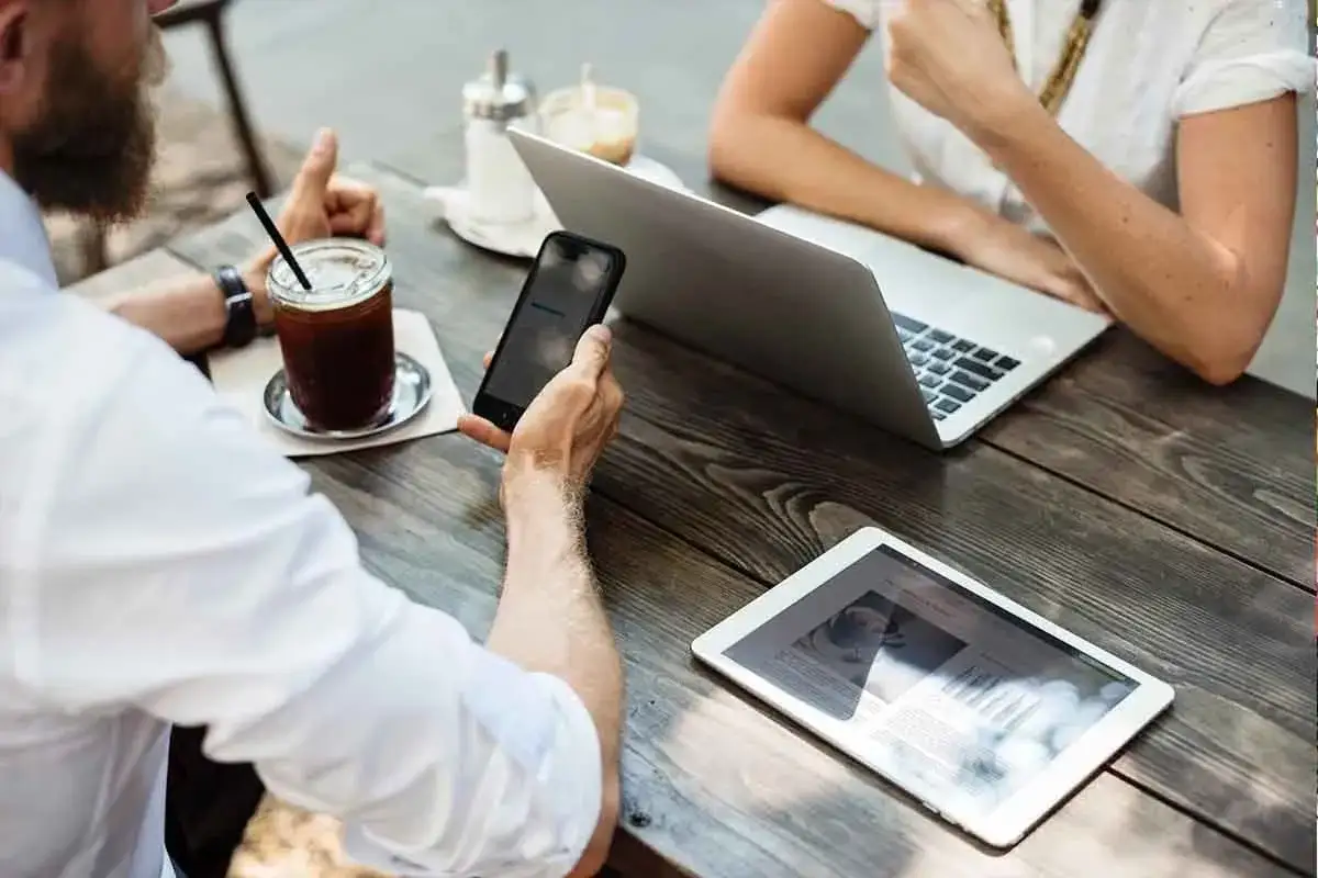 Dos personas trabajando en un café, con un portátil, tablet y móvil. Un ejemplo de trabajo nómada digital.