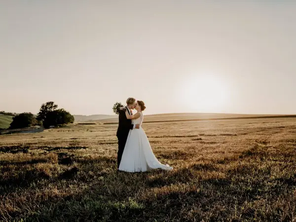 Novios besándose en un campo dorado al atardecer, un hermoso escenario para bodas en mayo.