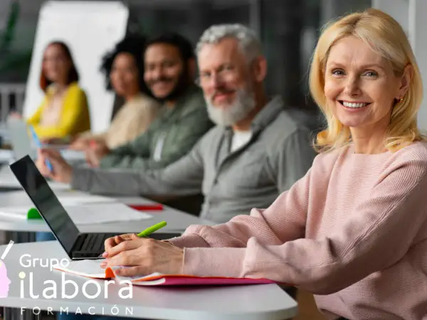 Mujeres y hombres participan en un curso formador de formadores online. Sonríen mientras aprenden en un aula moderna.